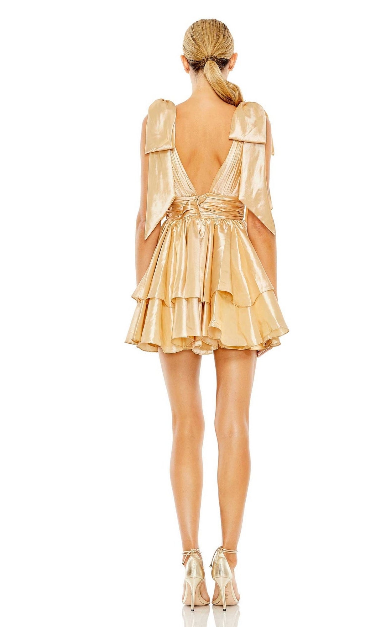 A woman faces away, wearing the Bow Short Ruffled Hoco Dress: Mac Duggal 11657 in shiny gold with a deep V-back and ruffles. She pairs it with matching heels, her hair styled in a low ponytail.